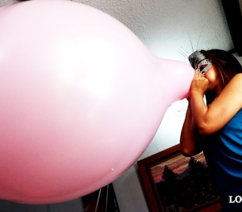 Alexis blowing up a Giant Pink Balloon in blue shorts.
